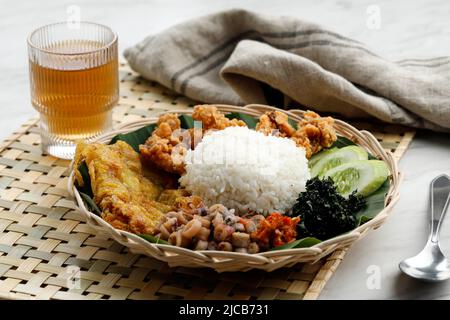 Ausgewählter Fokus Nasi Campur Cumi-Ase, Weißer Reis mit sautiertem gesalzenem Tintenfisch, Sambal, Ei, Kulit Ayam knusprige Hühnerhaut und gekochtes Cassava-Blatt. Stockfoto