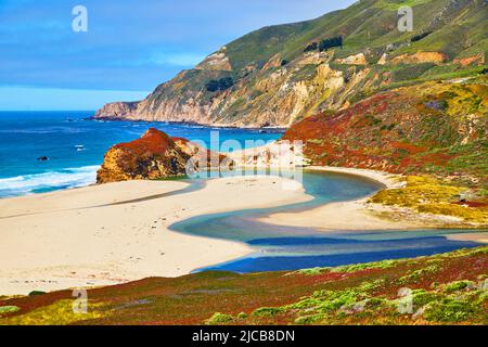 Der majestätische blaue Fluss am Meeresstrand trifft auf das Meer, umgeben von Hügeln, die von Frühlingspflanzen bedeckt sind Stockfoto