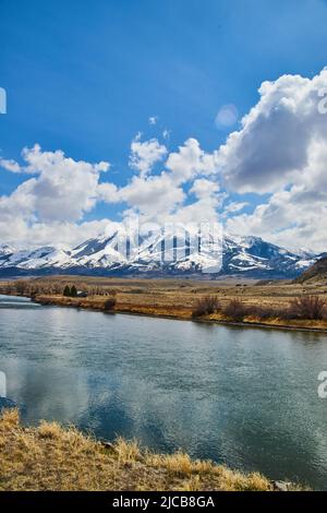Fluss und Felder mit verschneiten Bergen und blauem Himmel Stockfoto
