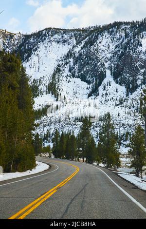 Straße, die durch verschneite Berge in Yellowstone führt Stockfoto