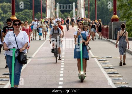 Kiew, Ukraine. 11.. Juni 2022. Ukrainer werden an einem heißen, sonnigen Tag in einer Altstadt von Kiew gesehen, wie sie eine Fußgängerbrücke über den Fluss Dnipro überqueren. Als die Russische Föderation vor 3 und einem halben Monat in die Ukraine einmarschierte, dauern die heftigen Kämpfe im Osten des Landes an. Die Hauptstadt Kiew bleibt in relativer Sicherheit, und die Bevölkerung beansprucht den öffentlichen Raum und ebnet den Weg zur Normalisierung. Kredit: SOPA Images Limited/Alamy Live Nachrichten Stockfoto