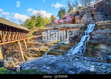 Atemberaubende Wasserfälle, die im Frühjahr unter einer Holzbrücke ins Tal hinunterstürzen Stockfoto