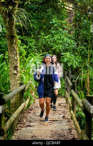 La Estrella, Antioquia, Kolumbien - Februar 13 2022: Eine braune Frau mit einem Schmetterlingskopftuch isst ein Sandwich, während sie auf einer Holzbrücke läuft Stockfoto