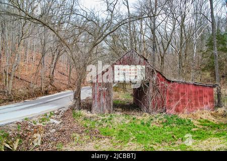 Rote Scheune mit Vintage-Schild neben der Straße im Frühjahr Stockfoto