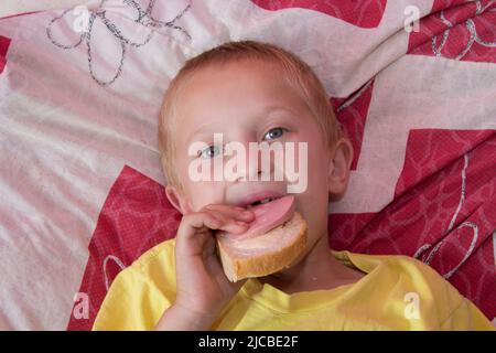 Draufsicht auf einen Jungen, der Sandwiches isst, während er im Bett liegt Stockfoto