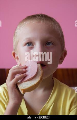 Überrascht Junge essen gekochte Wurst mit Brot Stockfoto