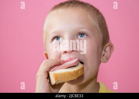 Junge mit blauen Augen isst Brot mit gekochter Wurst Stockfoto