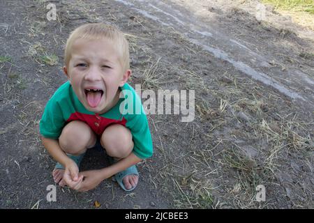 Boy zeigt Zunge auf dem Boden sitzen Stockfoto