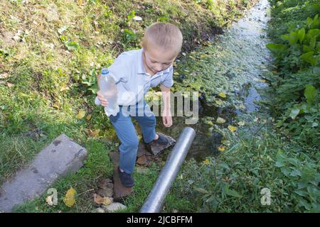 Boy geht aus der Quelle mit einer vollen Flasche Wasser Stockfoto