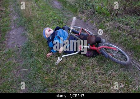 Boy fiel vom Fahrrad auf der Straße in einem Feld Stockfoto