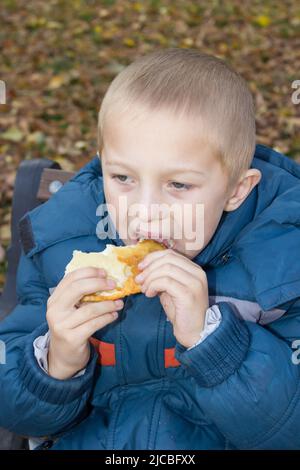 Hungriger Junge, der im kalten Herbst ein Stück Brot isst Stockfoto