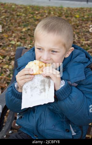 Porträt eines Jungen, der im Herbst ein heißes Sandwich isst Stockfoto