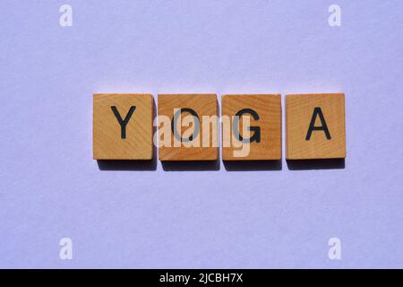 Yoga, Wort in Holzbuchstaben isoliert auf violettem Hintergrund Stockfoto
