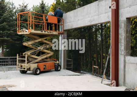 Scherenhubbühne mit Arbeitern auf einer Baustelle. Gebäude bauen Haus mit mobilen Transportfahrzeugen. Industrielle Maschine für die Arbeit Stockfoto