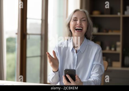 Ältere Frau hält Smartphone lachend Genießen Sie neue lustige mobile Anwendung Stockfoto