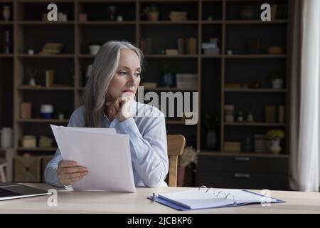 Eine attraktive, brütende Geschäftsfrau hält Papiere am Schreibtisch Stockfoto