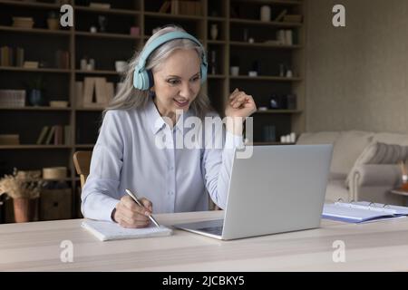 Frau sitzt am Schreibtisch mit Laptop hören Kurs Notizen schreiben Stockfoto