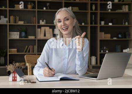 Ältere makler schreiben in Organizer, zeigt Thumbsup Blick auf die Kamera Stockfoto