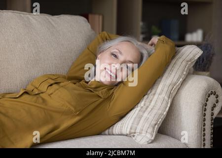 Schöne alte Frau, die auf der Couch liegt und lächelt, schaut auf die Kamera Stockfoto