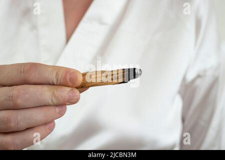 Frau Hand hält einen Stock des heiligen palo santo Holz, brennend. Weißer Satin Hintergrund. Stockfoto