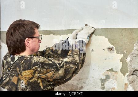 Entfernen von Farbe von der Wand mit einem Schaber, Reparatur des Raumes Stockfoto