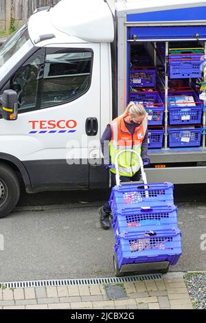 Tesco Supermarkt Online-Shopping-Lieferung weibliche Transporterfahrerin in gut sichtbarer Personaluniform schiebt Kunden-Food-Trolley außerhalb des Hauses England Großbritannien Stockfoto