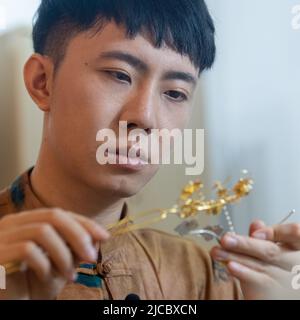 (220612) -- CHONGQING, 12. Juni 2022 (Xinhua) -- Gu Guoqiang macht ein filigranes Mosaikkunstwerk im südwestchinesischen Chongqing, 9. Juni 2022. Filigrane Mosaic Craft, ein traditionelles chinesisches aulic Handwerk aus der Frühlings- und Herbstperiode (770-476BC), verwendet Metall wie Gold und Silber, um Kunstwerke mit Edelstein oder Perle einzufalten. Es wird auch als feines Gold Handwerk, da es in der Regel gesponnene Gold so dünn wie 0,16 Millimeter verwendet, um verschiedene Formen zu bilden, und wurde als eines der nationalen immateriellen kulturellen Erbe Chinas im Jahr 2008 aufgeführt. GU Guoqiang, geboren 1994, verliebte sich in das Handwerk Seven y Stockfoto