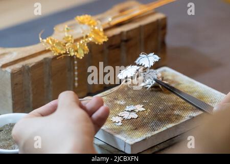 (220612) -- CHONGQING, 12. Juni 2022 (Xinhua) -- Gu Guoqiang macht ein filigranes Mosaikkunstwerk im südwestchinesischen Chongqing, 9. Juni 2022. Filigrane Mosaic Craft, ein traditionelles chinesisches aulic Handwerk aus der Frühlings- und Herbstperiode (770-476BC), verwendet Metall wie Gold und Silber, um Kunstwerke mit Edelstein oder Perle einzufalten. Es wird auch als feines Gold Handwerk, da es in der Regel gesponnene Gold so dünn wie 0,16 Millimeter verwendet, um verschiedene Formen zu bilden, und wurde als eines der nationalen immateriellen kulturellen Erbe Chinas im Jahr 2008 aufgeführt. GU Guoqiang, geboren 1994, verliebte sich in das Handwerk Seven y Stockfoto