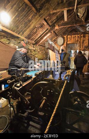 Mann, der mit Touristen in einem Blackhouse in Gearrannan in der Nähe von Carloway, Isle of Lewis, Äußere Hebriden, Schottland, Großbritannien, spricht Stockfoto