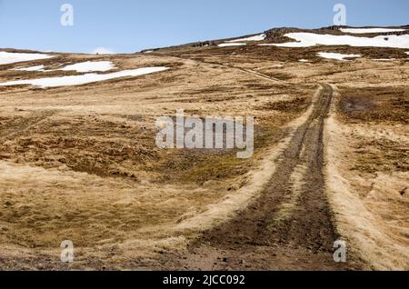 Unbefestigte Straße, die zu einem Pass in einem Gebiet mit niedrigen, teilweise schneebedeckten Bergen in der Nähe von Hvammstangi in Island führt Stockfoto