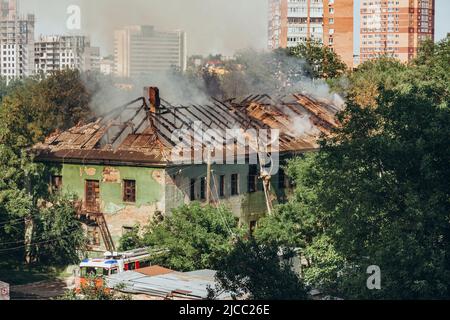 Russland, Rostow am Don - 2. Juni 2022: Feuerwehrleute stehen auf der Treppe und löschen einen Brand auf dem Dach eines verlassenen Hauses mit einem Hydranten. Stockfoto