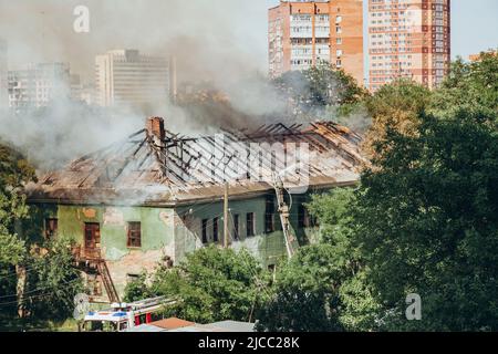 Russland, Rostow am Don - 2. Juni 2022: Feuerwehrleute stehen auf der Treppe und löschen einen Brand auf dem Dach eines verlassenen Hauses mit einem Hydranten. Stockfoto