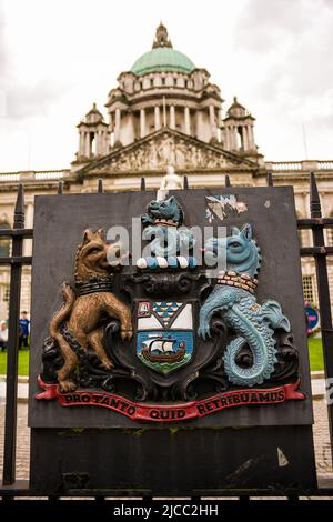 Belfast, Vereinigtes Königreich - 21. Mai 2022: Wappen als Relief auf einem eisernen Tor und im Hintergrund die Kuppel des Rathauses in Belfast, Northern IRE Stockfoto