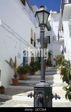 Frigiliana, Spanien. Ein weißes Dorf in den Bergen an der Costa del Sol. Enge steile Gasse mit Blumen im historischen maurischen Viertel. Vertikal sh Stockfoto