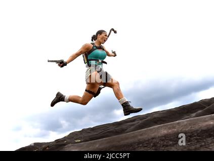 Ein junges Mädchen ist als Cosplay-Action-Superheldin Lara Croft gekleidet. Im Angriffsmodus wird sie im Freien in Aktion gesehen. Stockfoto