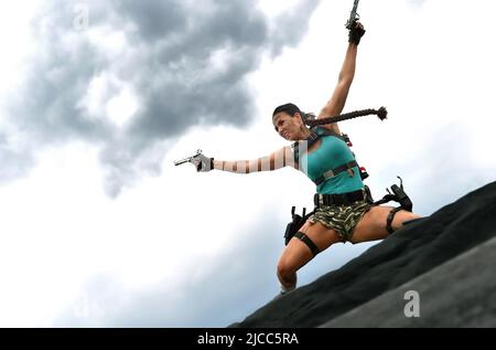 Ein junges Mädchen ist als Cosplay-Action-Superheldin Lara Croft gekleidet. Im Angriffsmodus wird sie im Freien in Aktion gesehen. Stockfoto