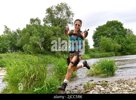 Ein junges Mädchen ist als Cosplay-Action-Superheldin Lara Croft gekleidet. Im Angriffsmodus wird sie im Freien in Aktion gesehen. Stockfoto