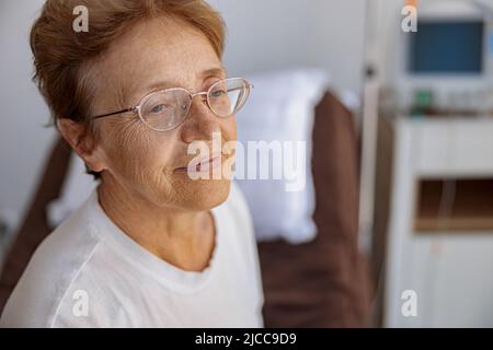 Lächelnde ältere Patientin auf der Station der modernen medizinischen Klinik, die wegschaut Stockfoto