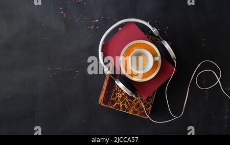 Hörbuchkonzept mit Bücherstapel, einer Tasse Espresso-Kaffee und Kopfhörern, die flach liegen, guter Platz für Kopien. Stockfoto