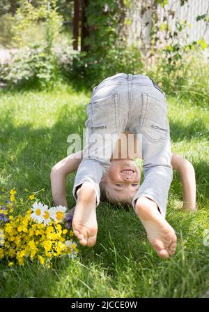 Barfuß Junge spielt draußen und steht fröhlich kopfüber auf dem Gras. Aktive Spiele für Kinder im Sommer, gesunde Lebensweise. Vorschulkinder haben Fu Stockfoto
