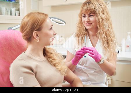 Elegante kaukasische Kosmetologin, die im Beauty-Center mit der Frau im Gespräch ist Stockfoto