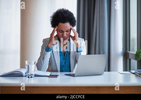 Müde junge Geschäftsfrau, die Kopfschmerzen hat. Eine Frau arbeitet an einem Laptop am Schreibtisch. Sie sitzt im Büro der Unternehmensleitung. Stockfoto