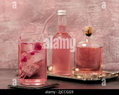 Ein Glas Pink Gin und Tonic, eine Flasche Rose Limonade und eine Flasche Pink Gin auf hellrosa Hintergrund Stockfoto