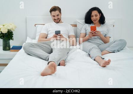 Lächelnder Mann und Frau mit Smartphones im Schlafzimmer Stockfoto