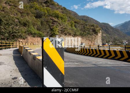 Eine Weitwinkelaufnahme einer wetterfesten Asphaltstraße mit gelben Betonbarrieren. Uttarakhand, Indien. Stockfoto