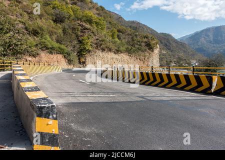 Eine Weitwinkelaufnahme einer wetterfesten Asphaltstraße mit gelben Betonbarrieren. Uttarakhand, Indien. Stockfoto