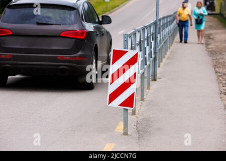 Rot und weiß diagonal gestreiftes Schild am Ende des Straßenzauns Stockfoto