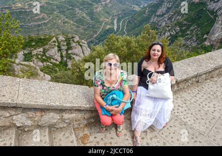 Porträt von Mutter und Tochter, die auf einer Brüstung in der Abtei Montserrat im Tal des Llobregat-Flusses im Hintergrund sitzen, Barcelona. Stockfoto