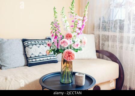 Frischer Strauß von Rosen und Füchshandschuhen Blumen in Vase im Wohnzimmer gelegt. Inneneinrichtung und Inneneinrichtung. Rosa orange blüht auf dem Tisch Stockfoto