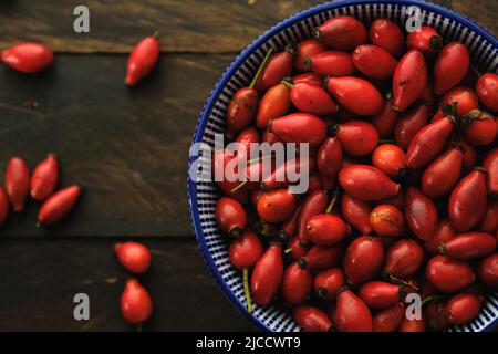 Eine Schüssel mit Hundsrosen (Rosa Canina) rote Hüften auf einem rustikalen Holztisch, Draufsicht Stockfoto